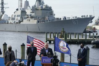 The USS Mason, an Arleigh Burke-class destroyer, glides past a news conference as former Gov. and Democratic gubernatorial candidate, Terry McAuliffe, at podium speaks, at Waterside in Norfolk, Va., Thursday, April 8, 2021. Virginia Gov. Ralph Northam, second from left, endorsed McAuliffe for governor. (AP Photo/Steve Helber)
