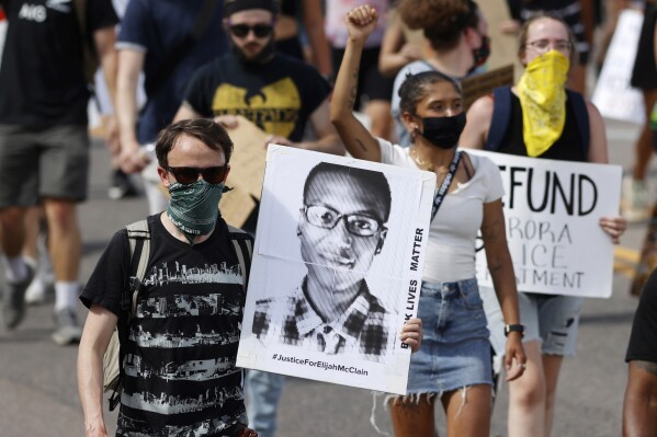 FILE - A demonstrator carries an image of Elijah McClain during a rally and march in Aurora, Colo., June 27, 2020. McClain, a 23-year-old Black man, died after a 2019 encounter with police. (AP Photo/David Zalubowski, File)