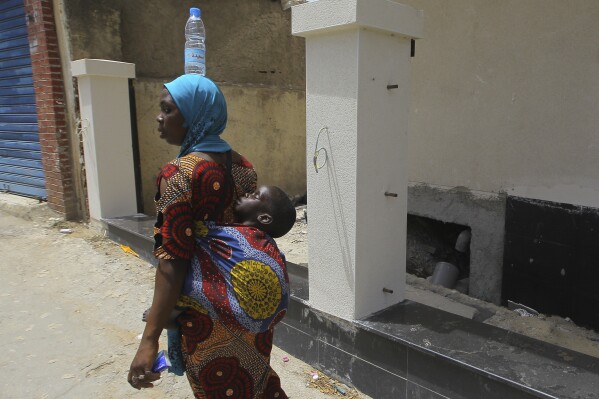 A woman from Niger carries her baby and a bottle of water on her head, Saturday, July 8, 2023. (AP Photo/Anis Belghoul)