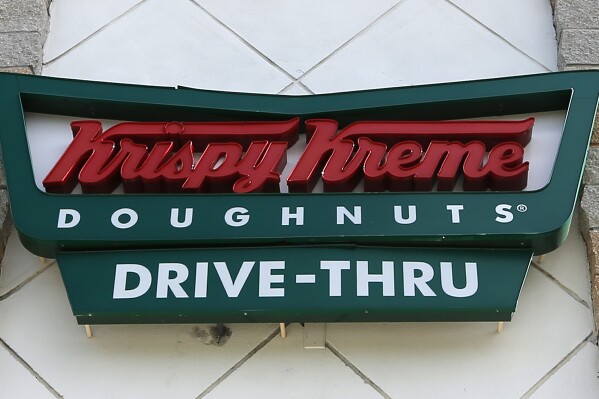 FILE - A Krispy Kreme Doughnuts sign is shown on Aug. 11, 2017, in Miami. More and more businesses are taking advantage of the total solar eclipse set to dim skies across North America on Monday, April 8, 2024. In the snacks department alone, Krispy Kreme is teaming up with Oreo to sell a limited doughnut-cookie creation. Sonic Drive-In is selling a “Blackout Slush Float.” (AP Photo/Alan Diaz, File)