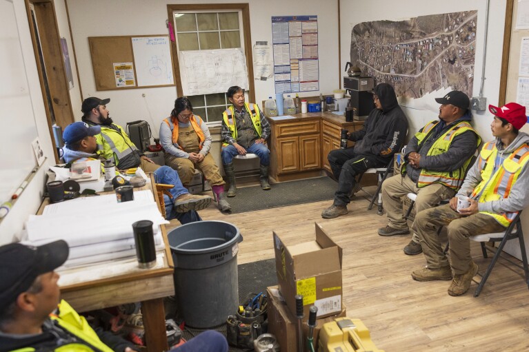 Alaska Native Tribal Health Consortium construction workers listen to Larry Le, center, during a morning meeting, Thursday, Aug. 17, 2023, in Akiachak, Alaska. (AP Photo/Tom Brenner)