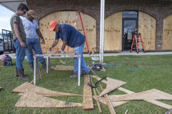 Bernie Arnould, center, gets help from Kaden Ashley and D.J. Hebert, left, all with Pelican Companies, as they board up the windows to the front of MC Bank in Amelia, La., Wednesday, Oct., 7, 2020, in In preparation for Hurricane Delta.  (Chris Granger/The Times-Picayune/The New Orleans Advocate via AP)