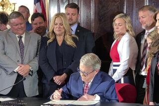 Gov. Mike DeWine signs "Collin's Law" to increase penalties for hazing during a ceremony on Tuesday, July 6, 2021, at the Statehouse in Columbus, Ohio. Standing immediately behind him among other lawmakers and guests were Wade and Kathleen Wiant, left, whose late son is the law's namesake, and Shari and Cory Foltz, right, whose son Stone died in March after another alleged fraternity hazing. (AP Photo/Kantele Franko)