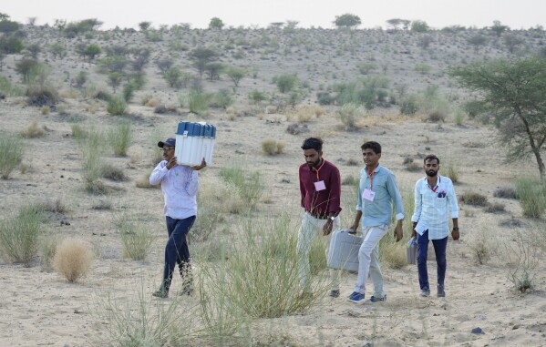 Polling officers carry an electronic voting machine and other election related material towards their assigned polling centre in a desert village on the eve of the second phase of polls in Akli village, in the western Indian state of Rajasthan, Thursday, April 25, 2024. (AP Photo/Deepak Sharma)
