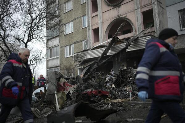 Workers pass the scene where a helicopter crashed on civil infrastructure in Brovary, on the outskirts of Kyiv, Ukraine, Wednesday, Jan. 18, 2023. The chief of Ukraine's National Police says a helicopter crash in a Kyiv suburb has killed 16 people, including Ukraine's interior minister and two children. He said nine of those killed were aboard the emergency services helicopter. (AP Photo/Daniel Cole)