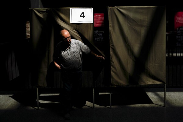 A person exits the voting booth with a ballot on the draft of a new constitution in Santiago, Chile, Sunday, Dec. 17, 2023. For the second time in as many years, Chileans vote in a referendum on whether to replace the current constitution which dates back to the military dictatorship of Gen. Augusto Pinochet. (AP Photo/Matias Basualdo)