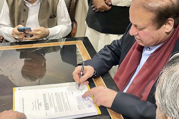 In this released by Pakistan Muslim League-N Party, Pakistan's former Prime Minister Nawaz Sharif, right, signs on the documents upon his arrival at Islamabad airport, Islamabad, Pakistan, on Saturday, Oct. 21, 2023. (Muslim League-N Party via AP)