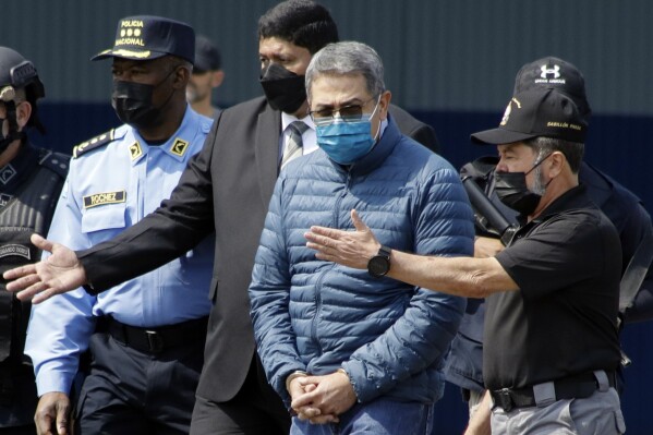 FILE - Former Honduran President Juan Orlando Hernandez, second from right, is taken in handcuffs to a waiting aircraft as he is extradited to the United States, at an Air Force base in Tegucigalpa, Honduras, April 21, 2022. Hernández has been convicted in New York, Friday, March 8, of charges that he conspired with drug traffickers, his military and police to enable tons of cocaine to make it unhindered into the United States. (AP Photo/Elmer Martinez, File)