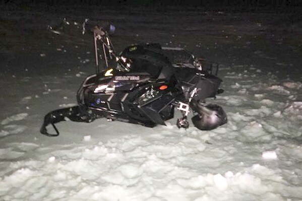 In this U.S. Army photograph by attorney Douglas Desjardins, a damaged snowmobile which crashed with a Black Hawk helicopter, March 13, 2019, in Worthington, Mass. A Massachusetts man wants the government to pay nearly $10 million after being badly injured in a crash with a Black Hawk helicopter. The lawsuit filed by Jeffrey Smith against the government follows a 2019 crash in which Smith's snowmobile collided with the helicopter that was parked on a trail at dusk. (U.S. Army photograph provided by attorney Douglas Desjardins via AP)