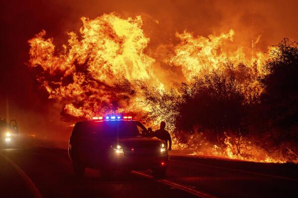 FILE - In this Sept. 9, 2020, file photo, flames lick above vehicles on Highway 162 as the Bear Fire burns in Oroville, Calif. Scientists say the outlook for the western U.S. fire season is grim because it's starting far drier than 2020's record-breaking fire year.(AP Photo/Noah Berger, File)
