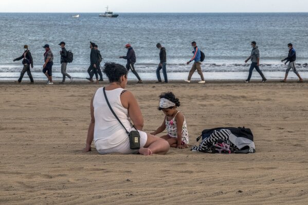 FILE - In this Tuesday, Oct.20, 2020 file photo, migrants from Morocco walk along the shore escorted by Spanish Police after arriving at the coast of the Canary Island, Spain. Overwhelmed authorities on the Canary Islands are on Wednesday, Nov. 11 asking Spain’s government for help to care for a rising number of migrants arriving from west Africa. Nearly 2,000 migrants are living in the facility designed to shelter 400 people on a pier on the island of Gran Canaria.  (AP Photo/Javier Bauluz)