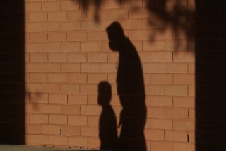 FILE - In this Friday, Oct. 9, 2020 file photo, the shadows of a school employee escorting a student are cast on the wall as they walk to a classroom on the first day of class at an elementary School in Davie, Fla. On Thursday, Jan. 14, 2021, top officials overseeing child welfare at the Department of Health and Human Services say they’ve seen no solid evidence to bear out warnings that serious forms of child abuse would surge during the coronavirus pandemic. (AP Photo/Wilfredo Lee)