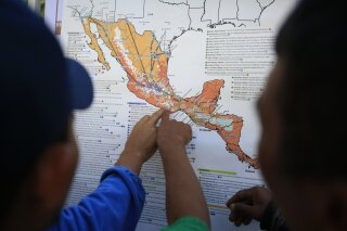 FILE - In this Nov. 9, 2018 file photo, migrants discuss their journey using a map posted inside the sports complex where thousands of migrants have been camped out for several days in Mexico City.  The United States began sending Honduran and Salvadoran asylum seekers to Guatemala in November 2019 and in Jan. 2020 said it would expand it to Mexicans. (AP Photo/Rebecca Blackwell, File)