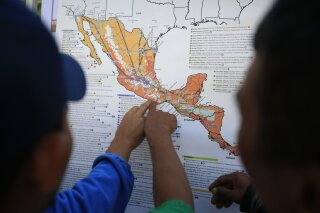 FILE - In this Nov. 9, 2018 file photo, migrants discuss their journey using a map posted inside the sports complex where thousands of migrants have been camped out for several days in Mexico City. The United States began sending Honduran and Salvadoran asylum seekers to Guatemala in November 2019 and in Jan. 2020 said it would expand it to Mexicans. (AP Photo/Rebecca Blackwell, File)