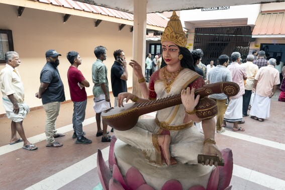 People queue up to vote behind a statue of the Hindu goddess of learning, Saraswati, during the second round of voting in the six-week long national election outside a polling booth in Kochi, southern Kerala state, India, Friday, April 26, 2024. (AP Photo/R S Iyer)