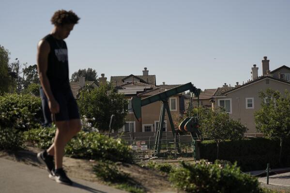 FILE - A man walks along the street as a pump jack extracts oil at a drilling site next to homes Wednesday, June 9, 2021, in Signal Hill, Calif. A California legislative committee has blocked a bill that would have made oil companies liable for the health problems of people who live close to oil wells. It's among dozens of bills that did not survive the legislature's suspense file hearings. (AP Photo/Jae C. Hong, File)