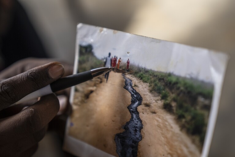 A man displays a photo he says shows toxic chemicals spilled due to oil drilling, in the village of Kinkazi, outside Moanda, Democratic Republic of the Congo, Sunday, Dec. 24, 2023. (AP Photo/Mosa'ab Elshamy)