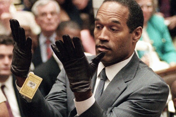 FILE - In this June 21, 1995 file photo, O.J. Simpson holds up his hands before the jury after putting on a new pair of gloves similar to the infamous bloody gloves during his double-murder trial in Los Angeles. Simpson, the decorated football superstar and Hollywood actor who was acquitted of charges he killed his former wife and her friend but later found liable in a separate civil trial, has died. He was 76. (Vince Bucci/Pool Photo via AP, File)