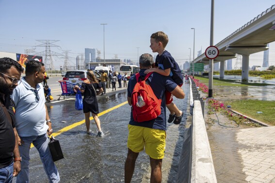 A man carries a child through floodwater caused by heavy rain while waiting for transportation on Sheikh Zayed Road highway in Dubai, United Arab Emirates, Thursday, April 18, 2024. The United Arab Emirates attempted to dry out Thursday from the heaviest rain the desert nation has ever recorded, a deluge that flooded out Dubai International Airport and disrupted flights through the world's busiest airfield for international travel. (AP Photo/Christopher Pike)