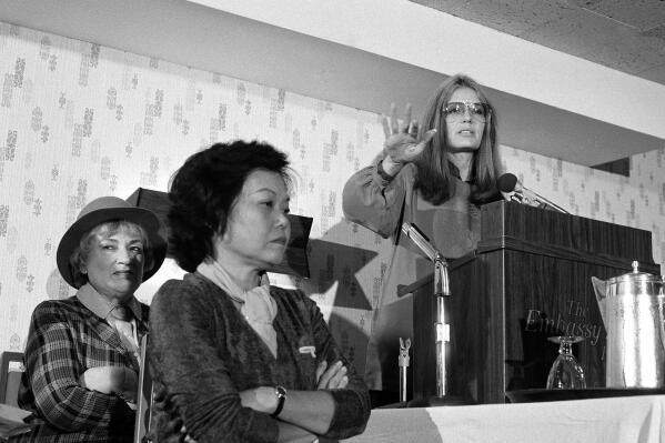 FILE - In this Nov. 21, 1979 file photo, Bella Abzug, left, and Patsy Mink of Women USA sit next to Gloria Steinem as she speaks in Washington where they warned presidential candidates that promises for women's rights will not be enough to get their support in the next election. Title IX, the law best known for its role in gender equity in athletics and preventing sexual harassment on campuses, is turning 50. It was signed into law by President Richard Nixon on June 23, 1972, after being shepherded through Congress in part by Rep. Patsy Mink, a Democrat from Hawaii who was the first woman of color elected to the U.S. House. (AP Photo/Harvey Georges, File)
