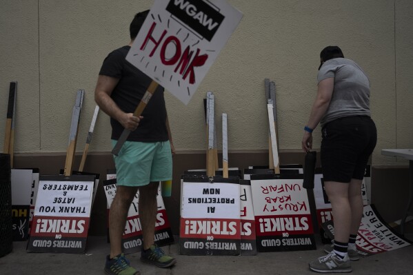 Two demonstrators pick up signs outside the Paramount Pictures Studio in Los Angeles, Thursday, Sept. 21, 2023. Negotiations between striking screenwriters and Hollywood studios have resumed and will continue Thursday, the latest attempt to bring an end to pickets that have brought film and television productions to a halt. (AP Photo/Jae C. Hong)