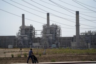 FILE - A man pushes a stroller near the AES power plant in Redondo Beach, Calif., Sept. 7, 2022. The California Energy Commission voted Wednesday, Aug. 9, 2023, to extend the life of three gas power plants along the state's southern coast through 2026, postponing a shutoff deadline previously set for the end of this year. The vote would keep the decades-old facilities — Ormond Beach Generating Station, AES Alamitos and AES Huntington Beach — open so they can run during emergencies. (AP Photo/Jae C. Hong, File)