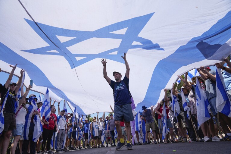 Demonstrators wave large Israeli flag during a protest against plans by Prime Minister Benjamin Netanyahu's government to overhaul the judicial system, outside the Knesset, Israel's parliament, in Jerusalem, Monday, July 24, 2023.  (AP Photo/Ohad Zwigenberg)