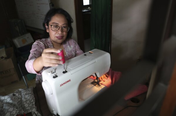 Parahita Satiti, who hopes to get extra income after her office cut her monthly allowance by half during the COVID-19 pandemic, makes traditional Javanese women's clothings in Jakarta, Indonesia, Thursday, Nov. 26, 2020. Satiti is one of dozens of tenants who joined online events run by Omah Wulangreh, an art and cultural community in Jakarta that provides online space for sellers and for buyers to preorder items like traditional snacks, batik clothes, or coffee. (AP Photo/Achmad Ibrahim)