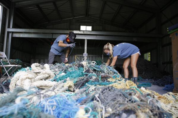 Hawaii Pacific University graduate student Drew McWhirter, left, and Raquel Corniuk, a research technician at the university's Center for Marine Debris Research, pull apart a massive entanglement of ghost nets on Wednesday, May 12, 2021 in Kaneohe, Hawaii. The two are part of a study that is attempting to trace derelict fishing gear that washes ashore in Hawaii back to the manufacturers and fisheries that it came from. (AP Photo/Caleb Jones)