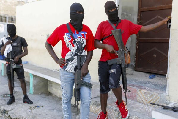 Masked members of "G9 and Family" gang stand guard during a press conference by their leader Barbecue in the Delmas 6 neighborhood of Port-au-Prince in Port-au-Prince, Haiti, Tuesday, March 5, 2024. Haiti's latest violence began with a direct challenge from Barbecue, a former elite police officer, who said he would target government ministers to prevent the prime minister's return and force his resignation. (AP Photo/Odelyn Joseph)