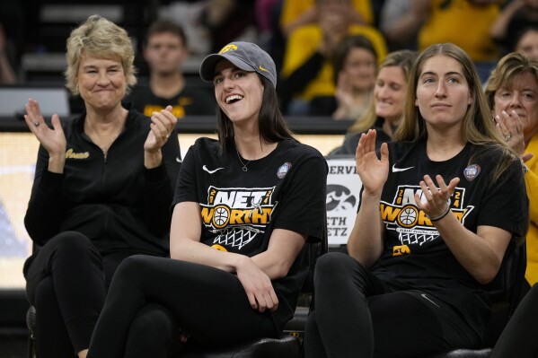 Iowa guard Caitlin Clark, center, sits with coach Lisa Bluder, left, and guard Kate Martin, right, as she finds out her number will be retired, during an Iowa women's basketball team celebration Wednesday, April 10, 2024, in Iowa City, Iowa. Iowa lost to South Carolina in the college basketball championship game of the women's NCAA Tournament on Sunday. (AP Photo/Charlie Neibergall)