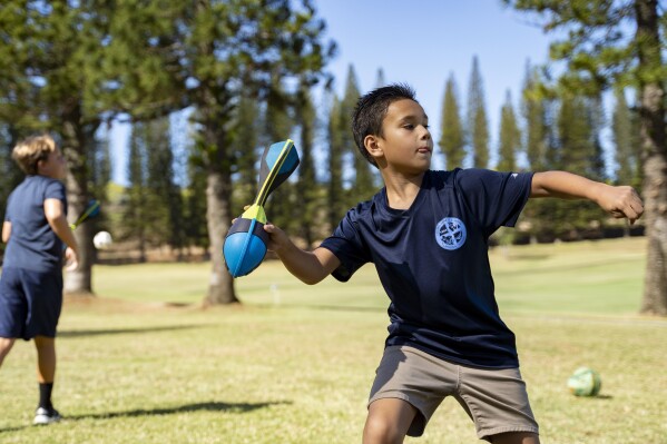 Sacred Hearts School third grade student Kupa'a Williams throws a ball during recess at a golf course at Kapalua Resort on Tuesday, Oct. 3, 2023, in Lahaina, Hawaii. The three public schools that survived the deadly August wildfire are set to reopen this week. (AP Photo/Mengshin Lin)