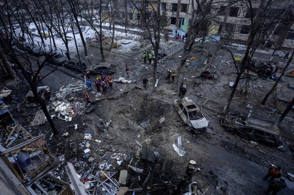 People stand near a crater in the yard of a damaged multi-store building after a Russian attack at residential neighbourhood in Kyiv, Ukraine, Wednesday, Dec. 13, 2023. (AP Photo/Evgeniy Maloletka)