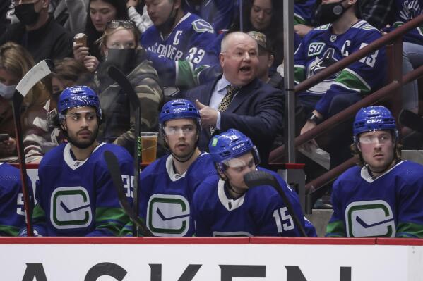 Vancouver Canucks head coach Bruce Boudreau, back, stands on the bench behind from left to right, Justin Bailey, Juho Lammikko, of Finland, Matthew Highmore and Brock Boeser while coaching in his 1,000th NHL game during the second period of an NHL hockey game against the St. Louis Blues in Vancouver, on Sunday, Jan. 23, 2022. (Darryl Dyck/The Canadian Press via AP)
