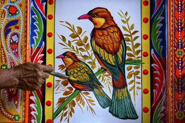 An artisan paints birds on a truck at a yard for workshops in Rawalpindi, Pakistan, on Saturday, April 19, 2025. (AP Photo/Anjum Naveed)