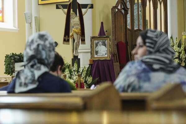 Parishioners sit around a photo of the late Pope Francis after the news of his death at age 88 at the Cathedral of the Immaculate Conception in Moscow, Russia, Monday, April 21, 2025. (AP Photo/Pavel Bednyakov)