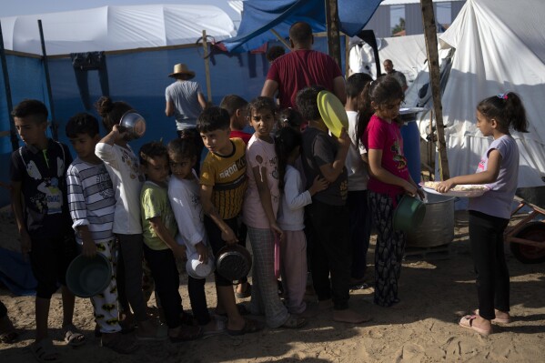 FILE - Palestinian children queue for a food distribution at a tent camp for displaced people, in Khan Younis, southern Gaza Strip, Wednesday, October 25, 2023. As the war between Israel and Hamas is in its second month and more than 10,000 people have been killed In Gaza, trapped civilians struggle to survive without electricity or running water.  Every day became a mind-numbing cycle of searching for bread and water and waiting in line.  A sense of hopelessness is straining Gaza's close-knit society.  (AP Photo/Fatima Shbair, file)