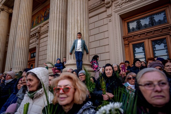 Children climb on a column to watch Romanian Orthodox priests and believers outside the Patriarchal Cathedral after an Orthodox Palm Sunday pilgrimage in Bucharest, Romania, Saturday, April 12, 2025. (AP Photo/Andreea Alexandru)