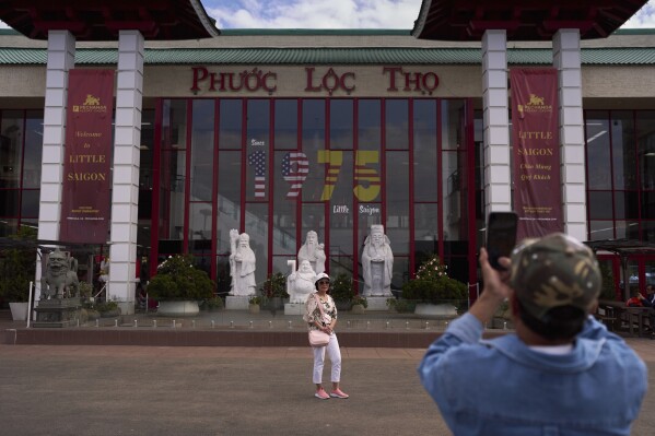A visitor poses for a photo in front of the Asian Garden Mall, which displays "1975" to mark the year of the fall of Saigon, in the Little Saigon neighborhood of Westminster, Calif., Friday, April 25, 2025. (AP Photo/Jae C. Hong)