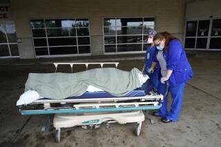 FILE - Medical staff prepare to move the body of a deceased COVID-19 patient to a funeral home van at the Willis-Knighton Medical Center in Shreveport, La., Wednesday, Aug. 18, 2021. Data released by the Centers for Disease Control and Prevention in April 2022 confirms that 2021 was the deadliest year in U.S. history. (AP Photo/Gerald Herbert, File)