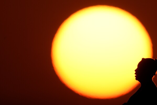 FILE - A woman is silhouetted against the setting sun as triple-digit heat indexes continue in the Midwest, Aug. 20, 2023, in Kansas City, Mo. Earth is exceeding its “safe operating space for humanity” in six of nine key measurements of its health, and two of the remaining three are headed in the wrong direction, a new study said. (AP Photo/Charlie Riedel, File)