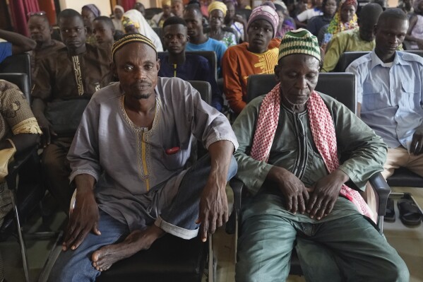 Community members sit in Materi town, Benin, Sunday, Oct. 8, 2023, waiting for a distribution of small portable stoves. Groups linked to al-Qaida and the Islamic State group have been spreading for years from the vast arid expanse south of the Sahara Desert — the Sahel — into wealthier West African coastal states like Benin. (AP Photo/Sam Mednick)