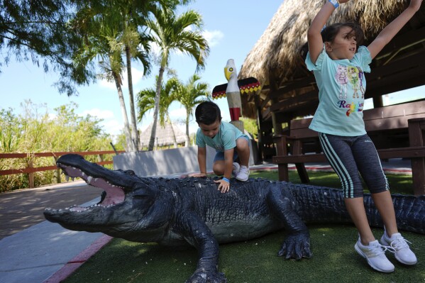 Lissandra Mendoza, 6, right, and her brother Saydel, 3, visiting from Miami with their family, play on an alligator statue during a day-long environmental and cultural education event at Miccosukee Indian Village, Saturday, April 20, 2024, in the Florida Everglades. The Earth Day event is one of many initiatives by tribe members aimed at building appreciation for the Everglades' unique and important ecosystem, as well as support to protect and heal it. (AP Photo/Rebecca Blackwell)