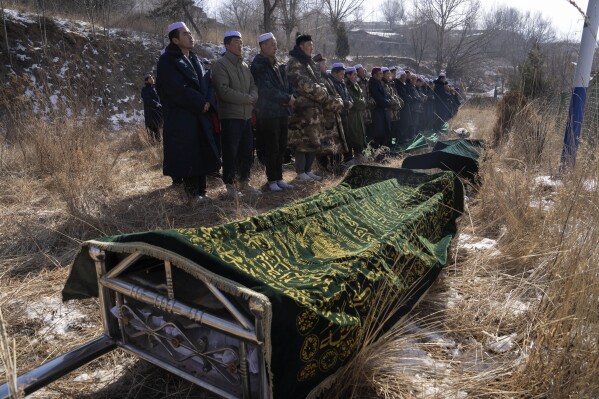 Ma Lianqiang, left, stands near the body of his wife Han Suofeiya who was killed in an earthquake before her burial at a cemetery in Yangwa village near Dahejia town in northwestern China's Gansu province, Wednesday, Dec. 20, 2023. (AP Photo/Ng Han Guan)
