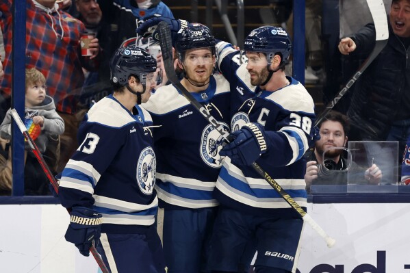 Columbus Blue Jackets forward Jack Roslovic, center, celebrates after his goal against the New York Rangers with teammates forward Johnny Gaudreau, left, and forward Boone Jenner, right, during the second period of an NHL hockey game in Columbus, Ohio, Sunday, Feb. 25, 2024. (AP Photo/Paul Vernon)