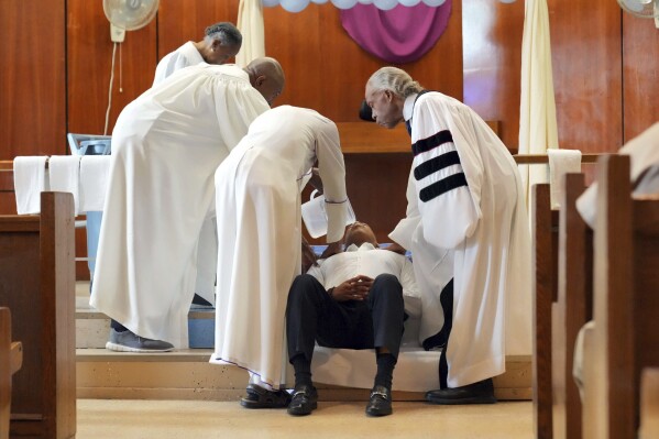 In this photo provided by the Office of the Mayor of New York, Mayor Eric Adams, second from right, laying back, participates in a baptism ceremony with Rev. Al Sharpton, right, while visiting the Rikers Island jail complex in New York, Friday, March 29, 2024. (Ed Reed/Mayoral Photography Office via AP)