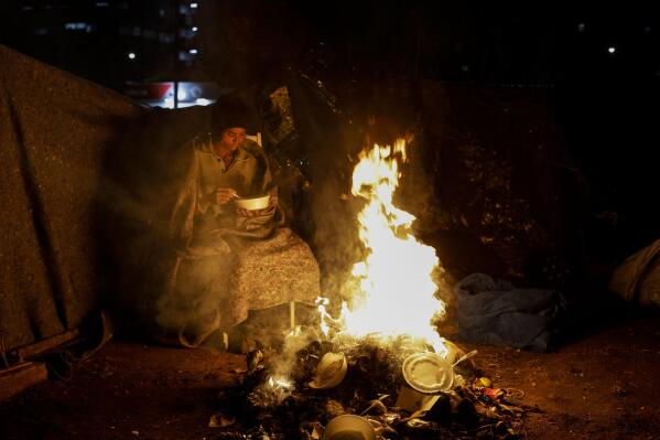 A homeless person sits by a fire amid historically cold weather in Sao Paulo, Brazil, late Thursday, July 29, 2021. The Brazilian government's meteorological institute says low temperatures should endure until the start of August. (AP Photo/Marcelo Chello)