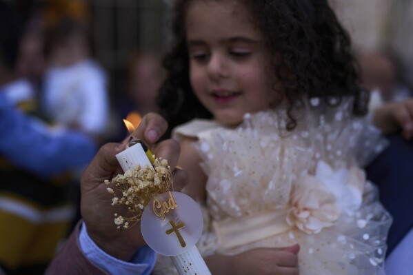 A man lights a candle for his daughter during Palm Sunday Mass at the Maronite Church of St. George in Quraye, near the southern port city of Sidon, Lebanon, Sunday, April 13, 2025. (AP Photo/Hassan Ammar)