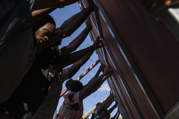 Neighbors raise a metal gate as they work to install it as a barricade against gangs, in the Petion-Ville neighborhood of Port-au-Prince, Haiti, Saturday, April 20, 2024. (AP Photo/Ramon Espinosa)