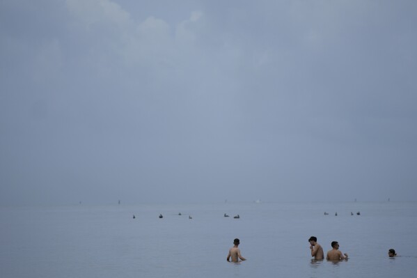 People swim in the ocean off of Crandon Park, Friday, July 28, 2023, in Key Biscayne, Fla. Humans naturally look to water for a chance to refresh, but when water temperatures get too high, some of the appeal is lost. (AP Photo/Rebecca Blackwell)